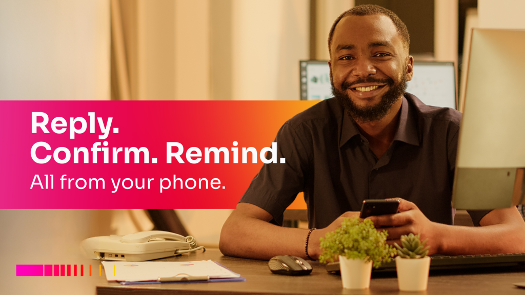Smiling freelancer holding a phone at his desk with the text 'Reply. Confirm. Remind. All from your phone' promoting Gebeya Jitume